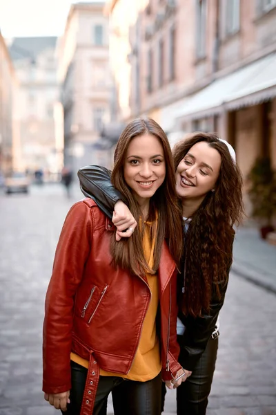 Lovable caucasian women in colored leather biker jackets and hoodies posing with smile on the street at autmn day. — Stock Photo, Image