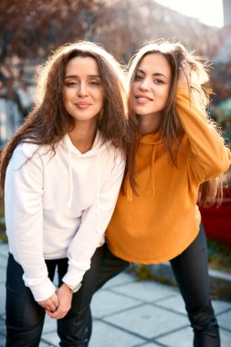 Siyah kapüşonlu sevimli beyaz kadınlar güz gününde sokakta gülümseyerek poz veriyorlar..