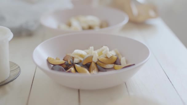 Cámara portátil. primer plano de frutas cortadas en bouls rosados para ensalada de frutas para un desayuno saludable. vista lateral superior de la mesa de madera blanca con ingredientes para el desayuno — Vídeo de stock