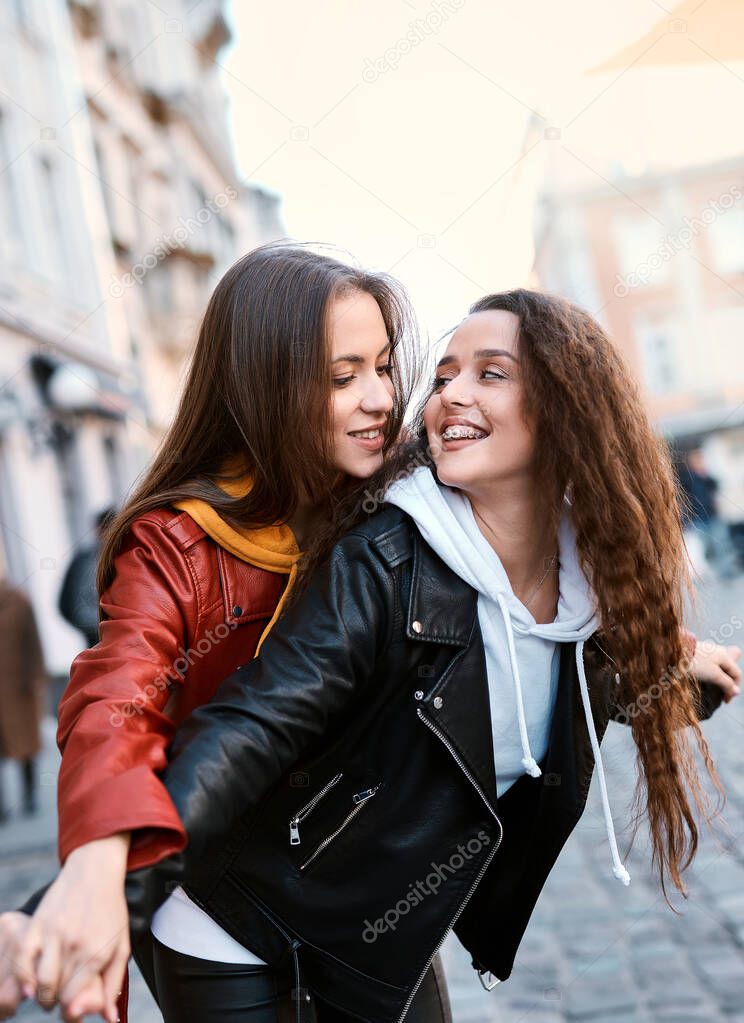 Smiling young lesbian couple embracing, looking at each other, walking in the street of the city at sunny autumn day.