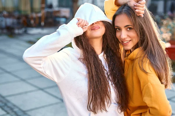 Retrato de jovencitas amigas graciosas en hoodias coloreadas con sonrisa en la calle en otoño día.. — Foto de Stock