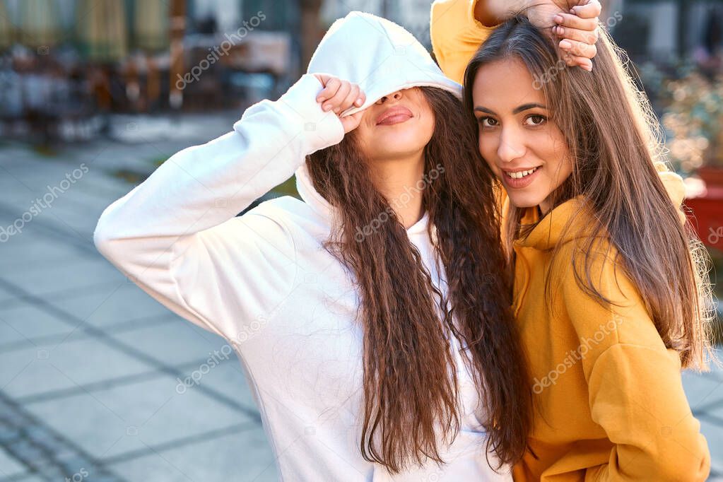 Portrait of funny girl friends in colored hoodies posing with smile on the street at autumn day.