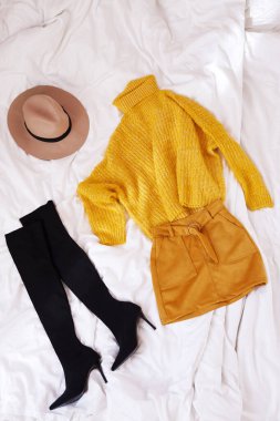 Kadın örgü sarı süveter, turuncu etek, şapka ve yüksek topuklu çizmeler, arka planda beyaz çarşaf. Sonbahar modasına uygun kadın kıyafetleri..