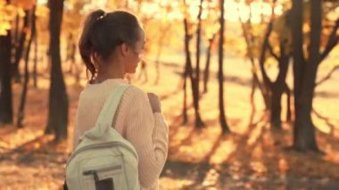 Genç bayan yürüyüşçü güneşli bir sonbahar gününde açık sonbahar ormanında yürüyor.