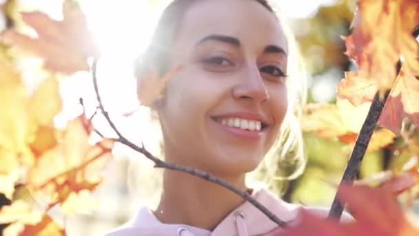 Close-up de bela jovem alegre sorrindo mulher olhando tromuto uma folhagem laranja brilhante na floresta de outono . — Vídeo de Stock