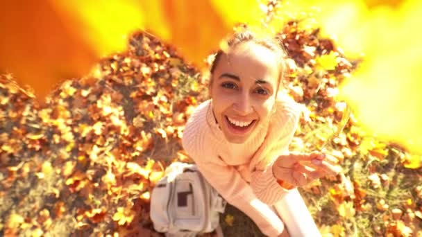 在秋天的森林里，美丽的年轻笑容满面的女子正看着一片鲜亮的橘红色树叶，她的特写镜头就在眼前. — 图库视频影像