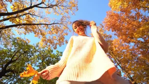 Vue du bas de joyeuse fille riante regardant vers le bas et jouant feuilles jaunes séchées . — Video