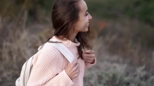 Nahaufnahme eines hübschen jungen Mädchens in gestricktem rosa Pullover mit kleinem Rucksack, das auf der Decke im Wald sitzt und lächelt. — Stockvideo