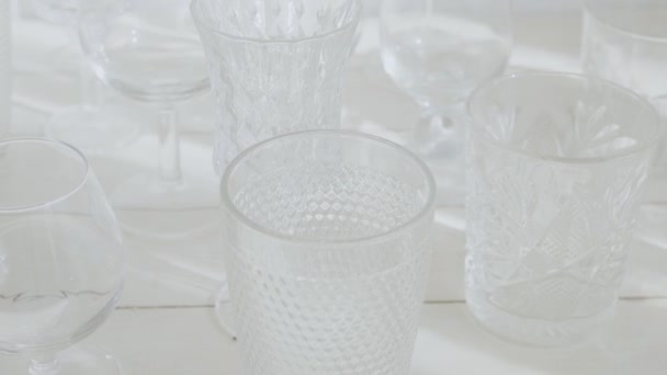 Many different transparent glasses on the white wooben table, top view — Stock Video