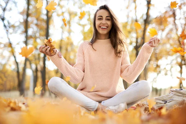 Cute smiling woman woman in autumn park, sitting on blanket, throwing autumn fall leaves. Fall concept. — Stock Photo, Image