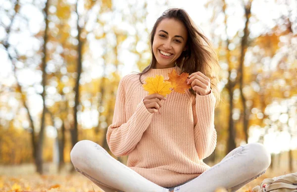 Cute smiling woman woman in autumn park, sitting on blanket, holding autumn leaves. Fall concept. — Stock Photo, Image