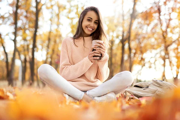 Søt, smilende kvinne i høstparken, sitter på et teppe, drikker kaffe, nyter varmt, solrikt vær. Fall-konsept . – stockfoto