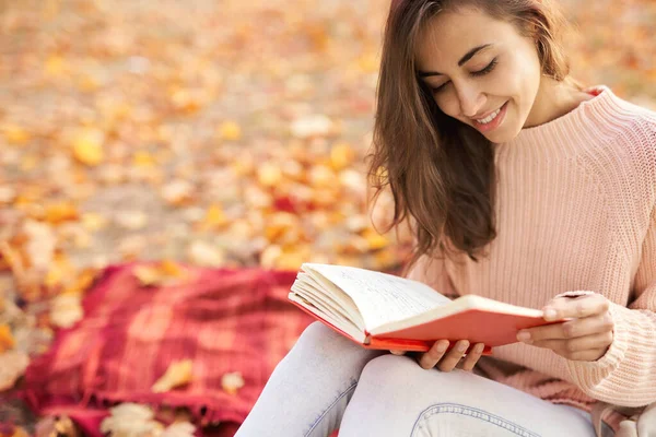 Portrait en gros plan d'une jolie femme souriante dans un parc d'automne, assise sur une couverture, lisant un journal intime. Concept d'automne . — Photo