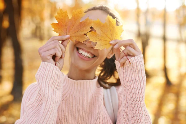 Autumn outdoor portrait of young smiling woman holding in her hands yellow maple leaves hiding her eyes in autumn park with colorful leaves on fall nature background. — Stock Photo, Image