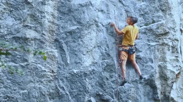 Man rotsklimmer begint te klimmen op een klif, zoeken, bereiken en grijpen greep. — Stockvideo