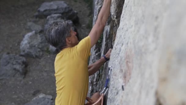 Młody człowiek alpinista zaczyna wspinać się na klif, szukając, docierając i chwytając chwyt. — Wideo stockowe