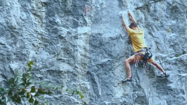 Чоловік скелястий альпініст починає підніматися по скелі, шукаючи, досягаючи і захоплюючи тримаючись . — стокове відео
