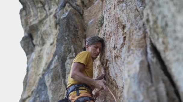 Ung man bergsklättrare börjar klättra på en klippa, söker, når och gripande grepp. — Stockvideo
