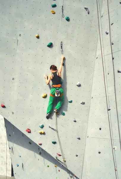 Achteraanzicht vrouw klimmer in fel groene broek klimmen op verticale kunstmatige rots muur. — Stockfoto