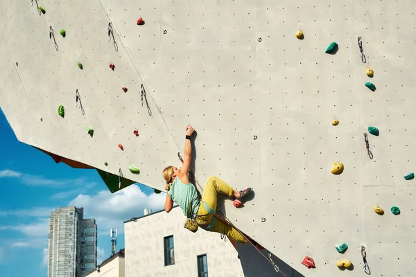 Jonge vrouw bergbeklimmer klimmen op kunstmatige rots muur in buiten klimmen sportschool. sport vrouw uit te werken op extra sport route. — Stockfoto