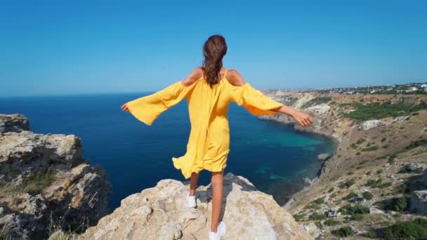 身披皮衣的女旅行家张开双臂站在岩石悬崖顶上的史诗般的慢动作 — 图库视频影像