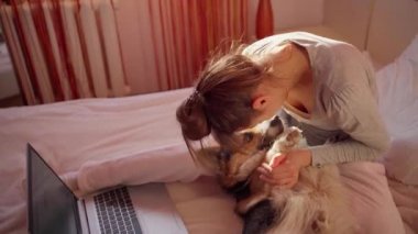 Nazik genç bir kadın yatakta sevimli bir köpeğe sarılıyor ve okşuyor.