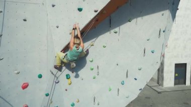 Spor salonunda tırmanma sporu yapan aktif bir kadın yapay kaya duvarında tırmanış yapıyor. Tutuyor, sert hareket ediyor ve sıkıca tutuyor..