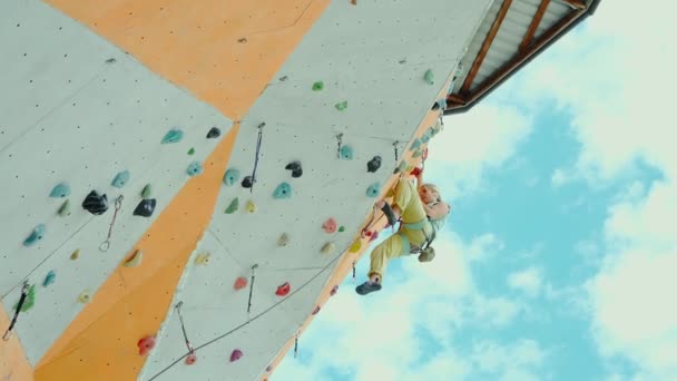 Sports woman climber practicing rock climbing on artificial rock wall in climbing gym, resting and chalking hands. — Stock Video