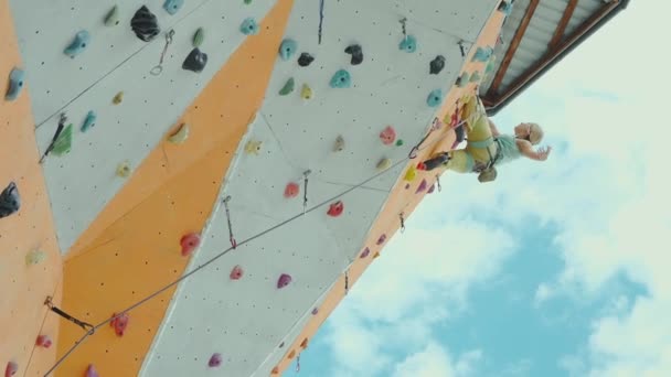 Woman climber in bright yellow pants climbing on artificial rock wall on outdoor climbing gym — Stock Video