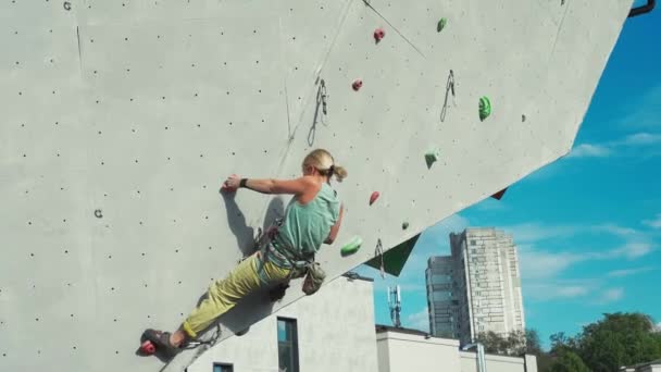 Young woman rock climber climbing on artificial rock wall in outside climbing gym. sports woman working out on extrime sport route. — Stock Video