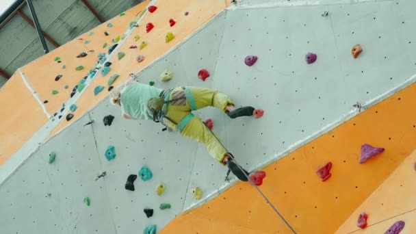 Fuerte escalador femenino escalada en pared vertical de roca artificial en el gimnasio de escalada exterior — Vídeos de Stock