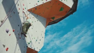 Spor salonunda tırmanma sporu yapan aktif bir kadın yapay kaya duvarında tırmanış yapıyor. Tutuyor, sert hareket ediyor ve sıkıca tutuyor..