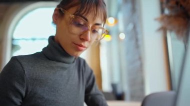Laptop 'ta, kafede kahve fincanıyla çalışan konsantre bir bayan öğrenci.
