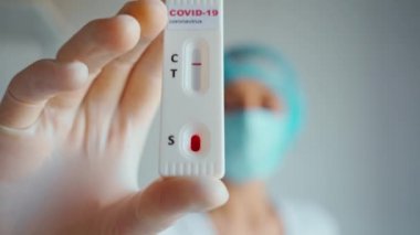Doktor ya da hemşire koruyucu yüz maskesi ve eldiven takıyor. Viral hastalık için laboratuvar kartı testi yapıyorlar. COVID-19