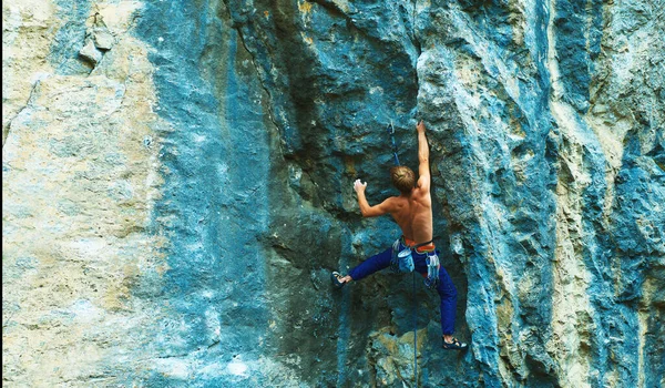 Rear view of strong man rock climber climbing the challenging route on the bright colorful rock cliff, making hard move. — Stock Photo, Image
