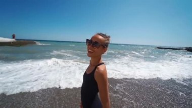 Kamera, mayo giyen mutlu zayıf kadını neşeyle dalgalanan denize doğru takip ediyor.