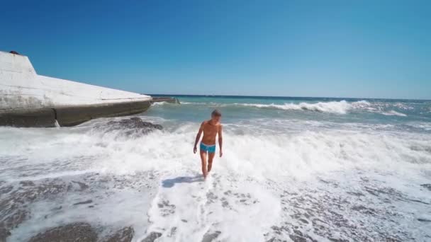 Atraente rindo homem bronzeado na praia com mar ondulante . — Vídeo de Stock