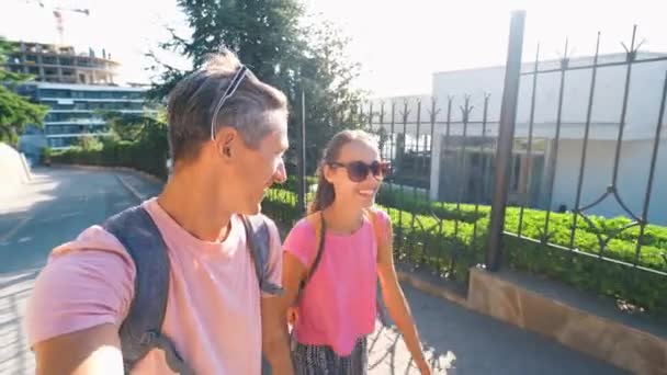 Young couple taking selfie portrait during walking sunny empty road with green fence — Stock Video