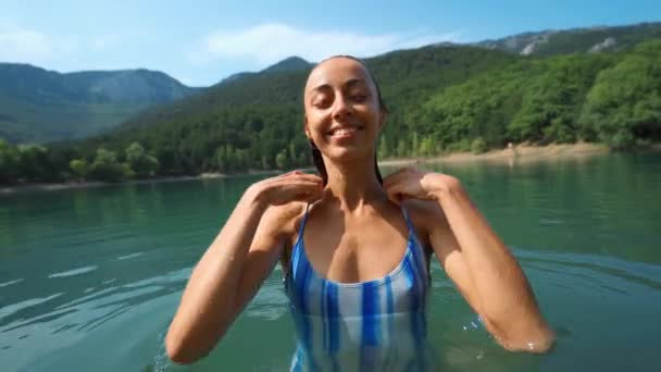 Mulher feliz bronzeada em roupa de banho azul sai do lago da montanha e esfregando o rosto com as mãos — Vídeo de Stock