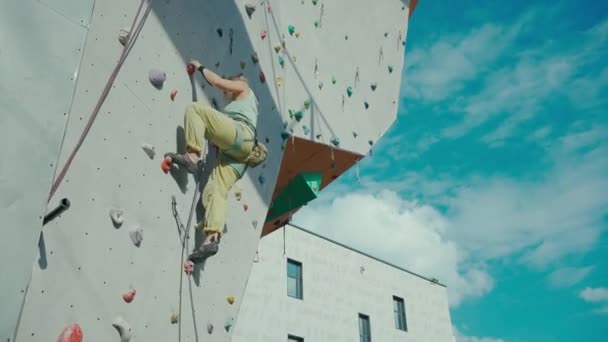 Visão traseira do atleta alpinista que se move para cima na parede de rocha artificial vertical . — Vídeo de Stock