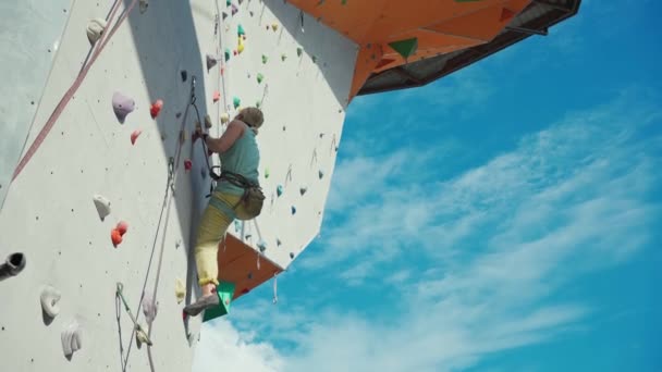Rear view of sportwoman climber moving up on vertical artificial rock wall. — Stock Video