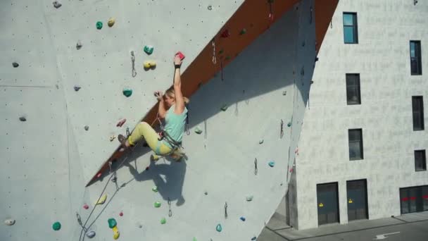 Sports girl climber climbing on artificial rock wall in outside climbing gym. Strong woman making hard move — Stock Video