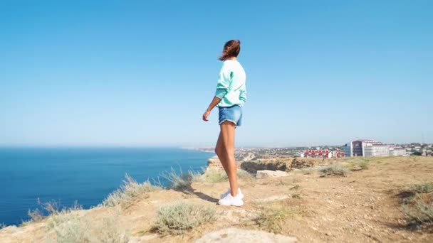 Bezstarostná mladá žena stojící se zdviženýma rukama na okraji útesu — Stock video