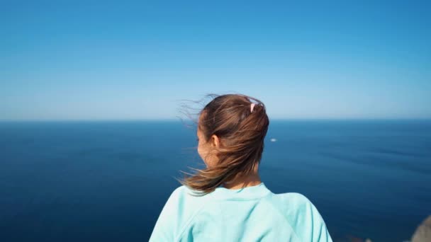 Jovem mulher de pé na borda alta penhasco sobre o mar desfrutando ensolarado manhã de verão — Vídeo de Stock