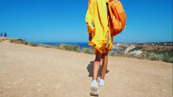 Câmera seguinte menina viajante em vestido de laranja e chapéu andando para precipitous borda do penhasco — Vídeo de Stock