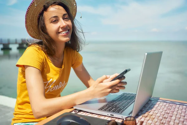 Onnellinen freelancer nainen hattu kannettava tietokone työskentelee rannalla, älypuhelimella ja internetissä — kuvapankkivalokuva