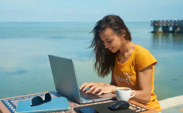 Naispuolinen freelancer työskentelee meren äärellä kannettavan tietokoneen avulla. Freelance-työn käsite — kuvapankkivalokuva