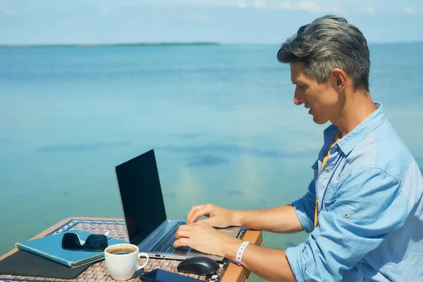 Homme d'affaires travaillant sur la plage le matin au bord de la mer, en utilisant un ordinateur portable. Liberté, télétravail, freelance, technologie, internet, voyages et vacances concepts — Photo