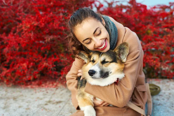 Söta stunder kvinna omfamna hennes vackra husdjur walesiska Corgi hund på hösten natur bakgrund med röda höstlöv — Stockfoto