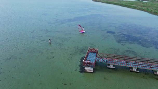 Imágenes aéreas de aviones no tripulados del instructor de windsurf enseñando a una mujer principiante a pararse en la tabla de surf — Vídeos de Stock